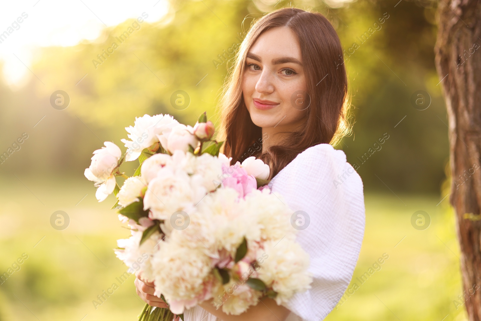 Beautiful woman with bouquet of peonies in park on sunny day Photo of Beautiful woman with bouquet of peonies in park on sunny day