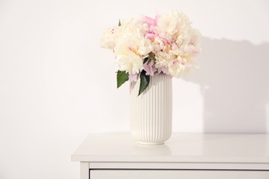 Photo of Bouquet of beautiful peonies on table near white wall