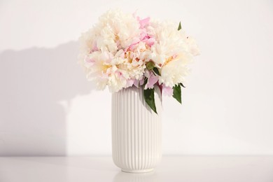 Photo of Bouquet of beautiful peonies on table near white wall