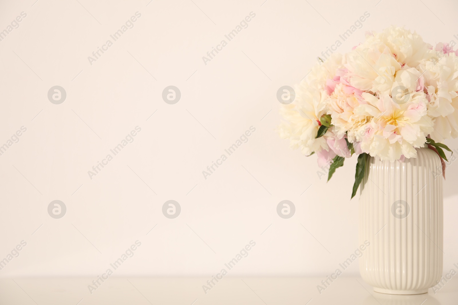 Bouquet of beautiful peonies on table near white wall. Space for text Photo of Bouquet of beautiful peonies on table near white wall. Space for text
