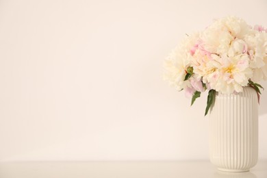 Photo of Bouquet of beautiful peonies on table near white wall. Space for text