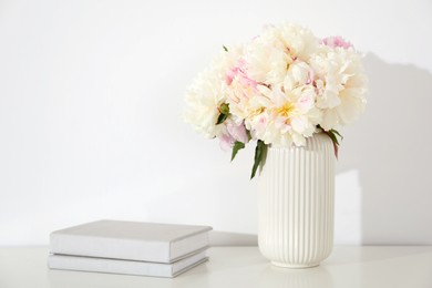 Photo of Bouquet of beautiful peonies and books on table near white wall. Space for text