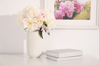 Photo of Bouquet of beautiful peonies and books on table indoors
