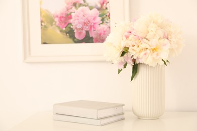 Photo of Bouquet of beautiful peonies and books on table indoors