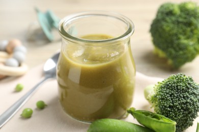 Photo of Baby food. Tasty puree in glass jar, ingredients and spoon on table, closeup