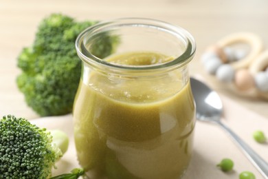 Photo of Baby food. Tasty puree in glass jar, ingredients and spoon on table, closeup