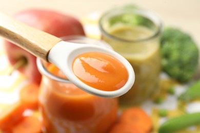 Photo of Baby food. Tasty puree in spoon, glass jars and ingredients on table, closeup