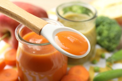 Photo of Baby food. Tasty puree in spoon, glass jars and ingredients on table, closeup