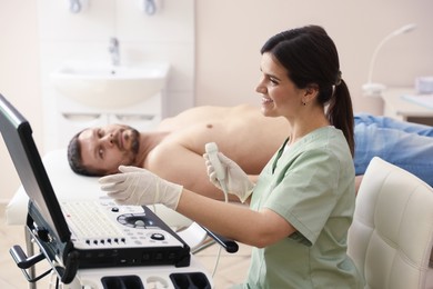 Photo of Sonographer with ultrasound transducer and man waiting for examination in clinic, selective focus