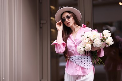 Photo of Stylish woman with bouquet of beautiful peonies outdoors. Space for text