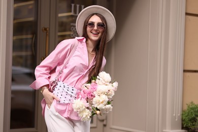 Photo of Stylish woman with bouquet of beautiful peonies outdoors. Space for text