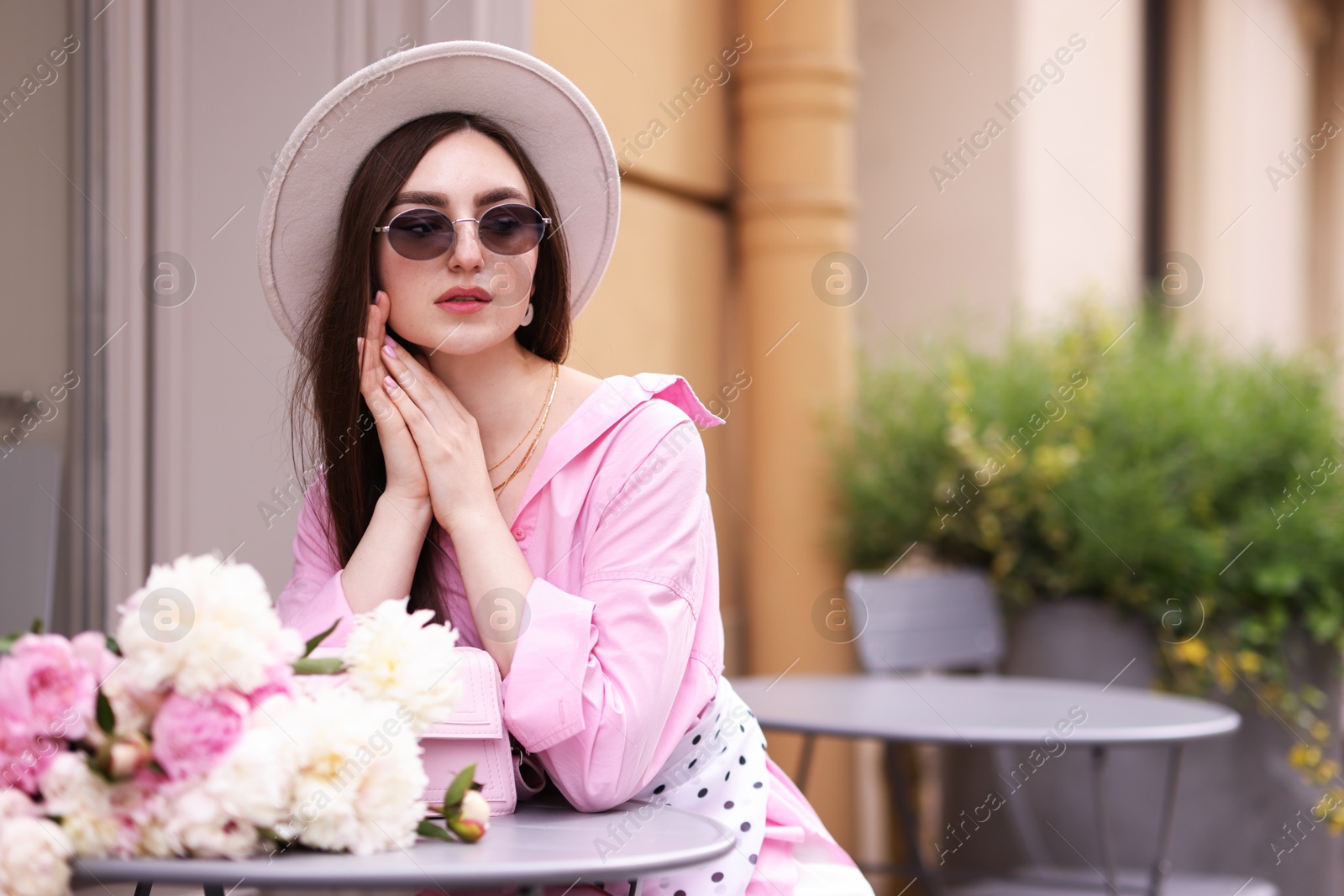 Photo of Stylish woman with beautiful peonies in outdoor cafe. Space for text