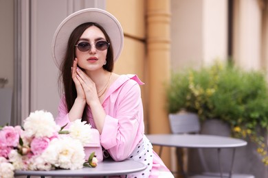 Photo of Stylish woman with beautiful peonies in outdoor cafe. Space for text