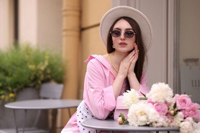 Photo of Stylish woman with beautiful peonies in outdoor cafe. Space for text