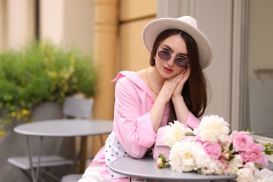 Photo of Stylish woman with beautiful peonies in outdoor cafe. Space for text