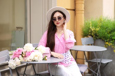 Photo of Stylish woman with beautiful peonies in outdoor cafe