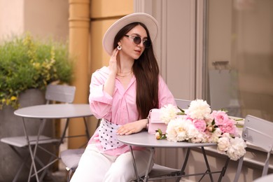 Photo of Stylish woman with beautiful peonies in outdoor cafe