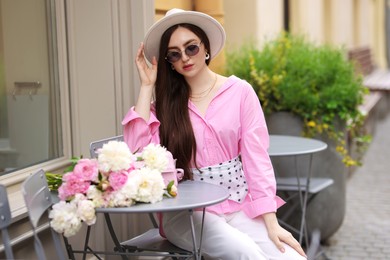 Photo of Stylish woman with beautiful peonies in outdoor cafe