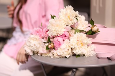 Photo of Stylish woman with beautiful peonies in outdoor cafe, closeup