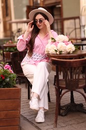 Photo of Stylish woman with beautiful peonies in outdoor cafe