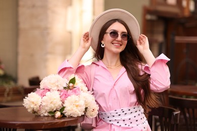 Photo of Stylish woman with beautiful peonies in outdoor cafe