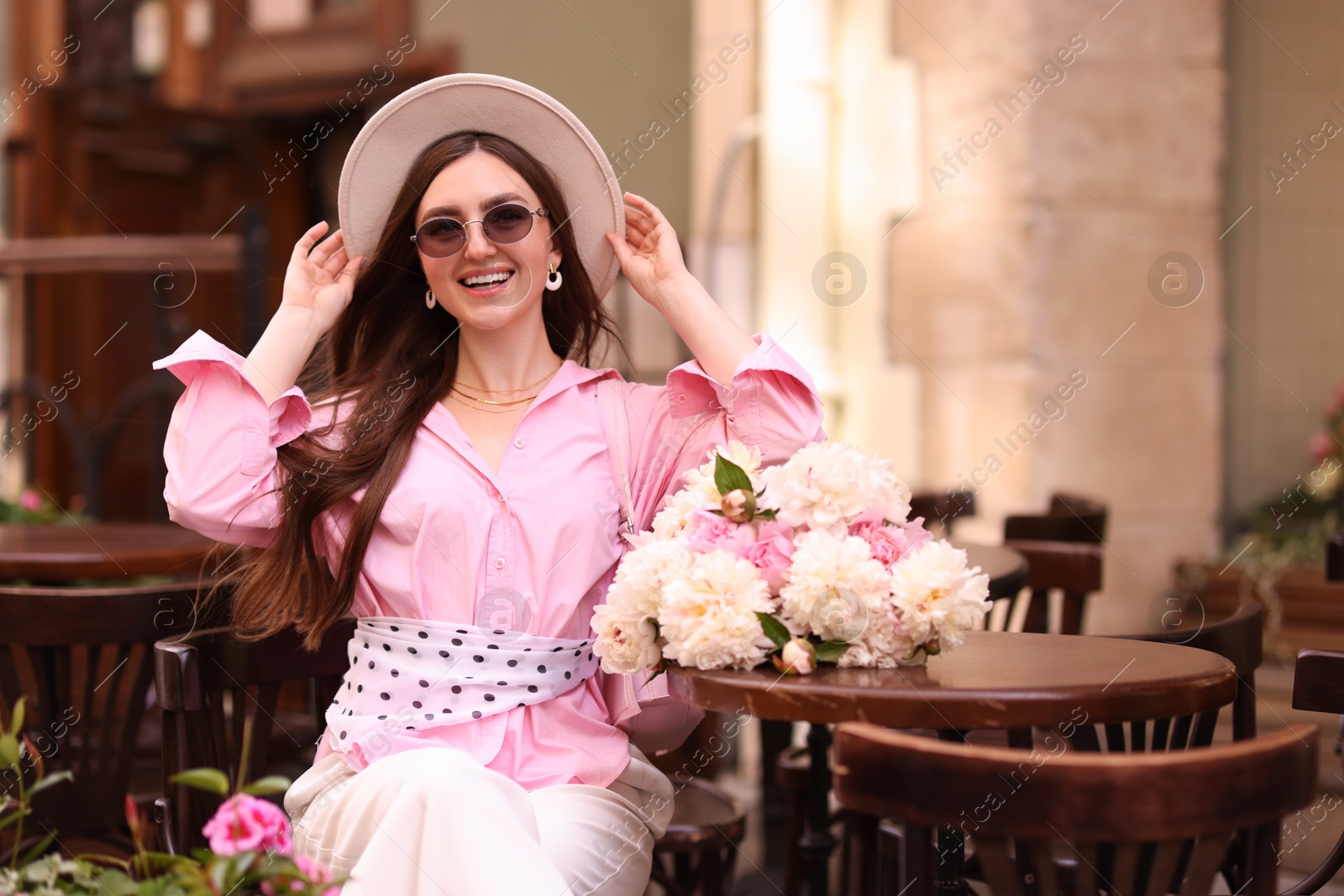 Stylish woman with beautiful peonies in outdoor cafe. Space for text Photo of Stylish woman with beautiful peonies in outdoor cafe. Space for text