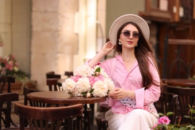 Photo of Stylish woman with beautiful peonies in outdoor cafe. Space for text
