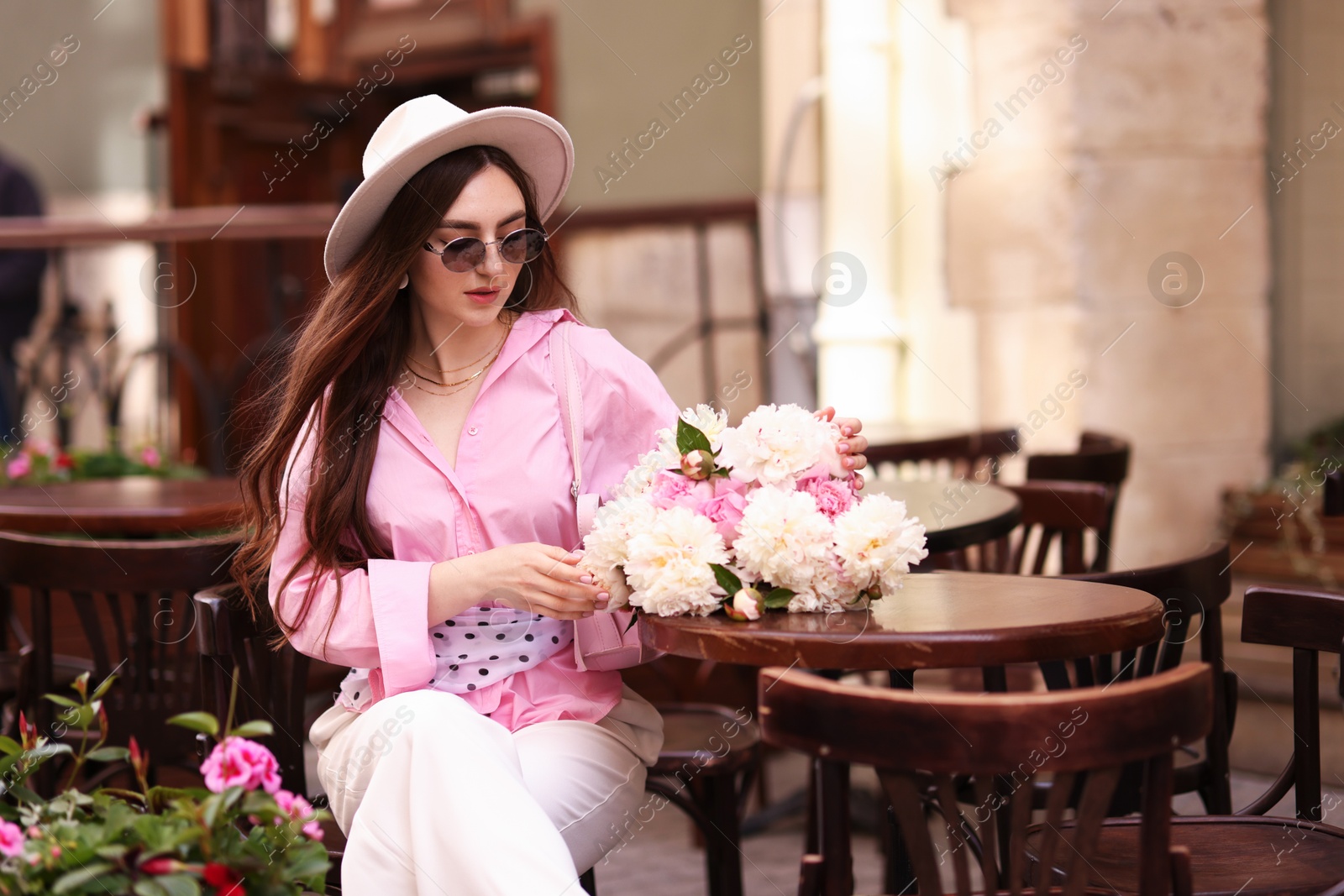 Stylish woman with beautiful peonies in outdoor cafe. Space for text Photo of Stylish woman with beautiful peonies in outdoor cafe. Space for text