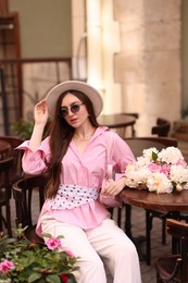 Photo of Stylish woman with beautiful peonies in outdoor cafe
