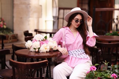 Photo of Stylish woman with beautiful peonies in outdoor cafe