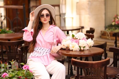 Photo of Stylish woman with beautiful peonies in outdoor cafe