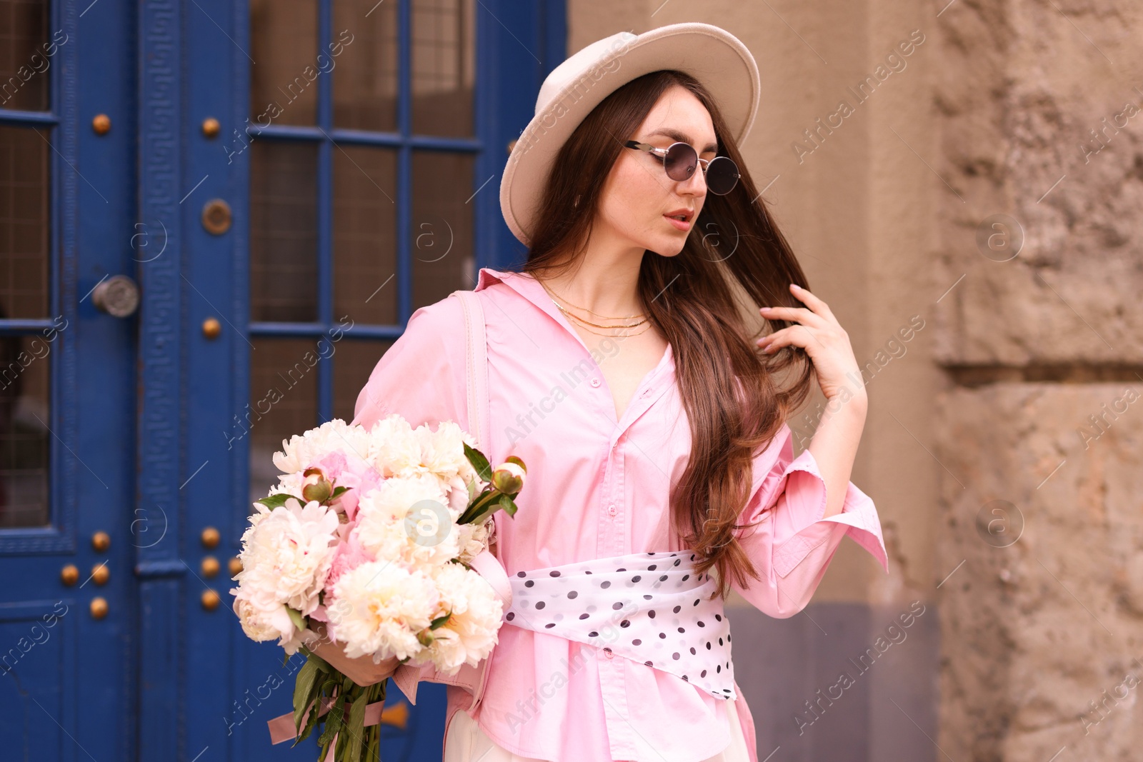 Stylish woman with beautiful peonies on city street Photo of Stylish woman with beautiful peonies on city street