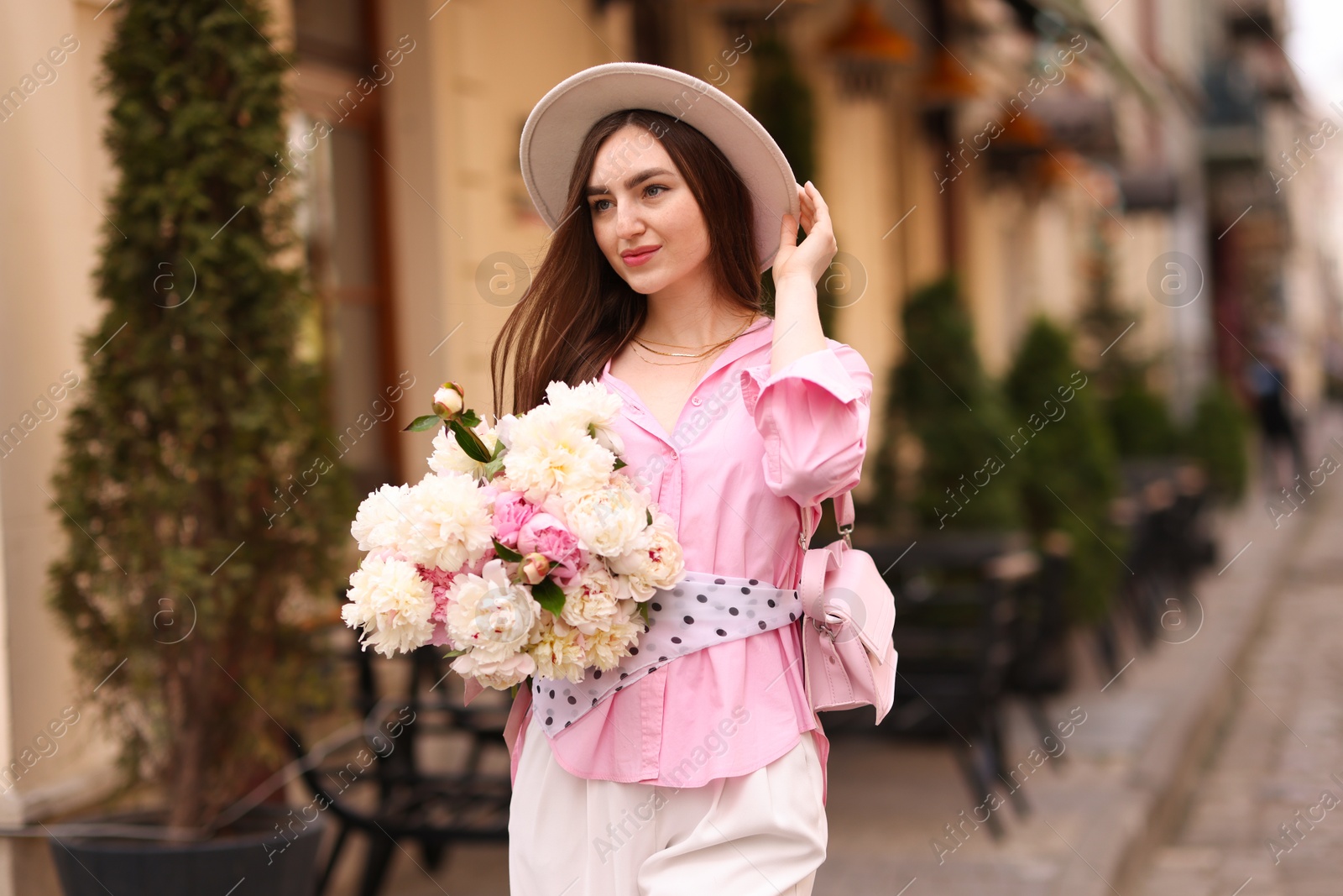Stylish woman with beautiful peonies on city street Photo of Stylish woman with beautiful peonies on city street