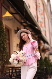 Photo of Stylish woman with beautiful peonies on city street. Space for text