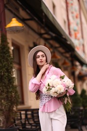 Photo of Stylish woman with beautiful peonies on city street. Space for text
