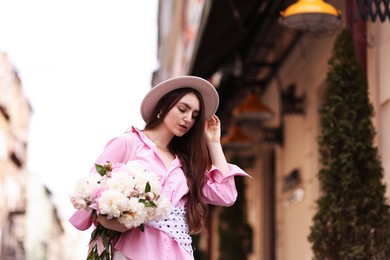 Photo of Stylish woman with beautiful peonies on city street. Space for text