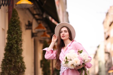 Photo of Stylish woman with beautiful peonies on city street. Space for text