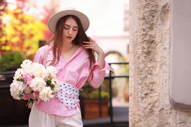 Photo of Stylish woman with beautiful peonies on city street. Space for text