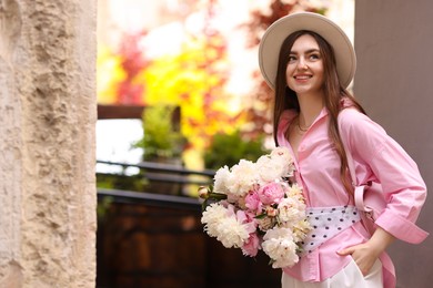 Photo of Stylish woman with beautiful peonies on city street. Space for text