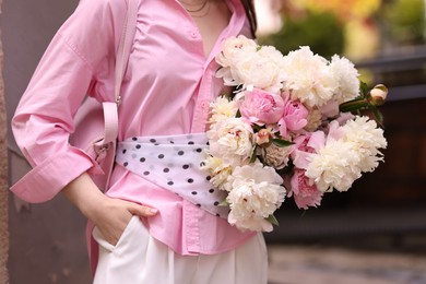 Photo of Stylish woman with beautiful peonies on city street, closeup
