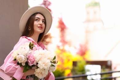 Photo of Stylish woman with beautiful peonies on city street. Space for text