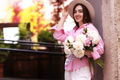 Photo of Stylish woman with beautiful peonies on city street. Space for text