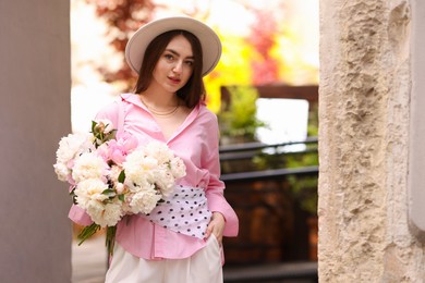 Photo of Stylish woman with beautiful peonies on city street. Space for text