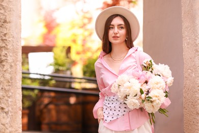 Photo of Stylish woman with beautiful peonies on city street. Space for text