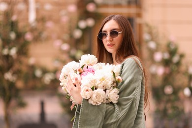 Photo of Charming woman with bouquet of beautiful peonies on city street. Space for text