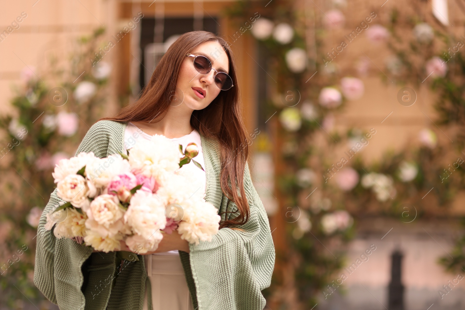 Charming woman with bouquet of beautiful peonies on city street. Space for text Photo of Charming woman with bouquet of beautiful peonies on city street. Space for text