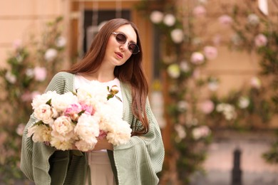 Photo of Charming woman with bouquet of beautiful peonies on city street. Space for text