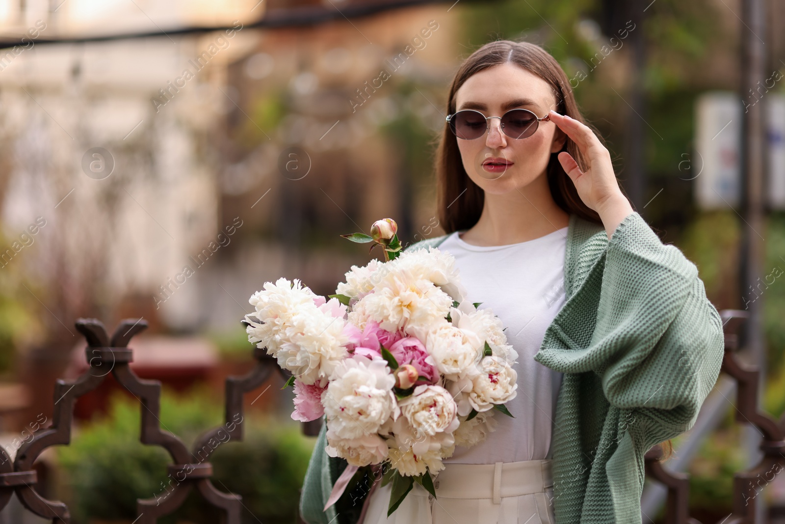 Charming woman with bouquet of beautiful peonies on city street. Space for text Photo of Charming woman with bouquet of beautiful peonies on city street. Space for text