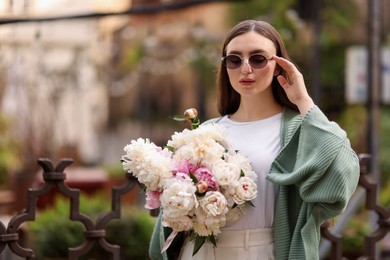 Photo of Charming woman with bouquet of beautiful peonies on city street. Space for text