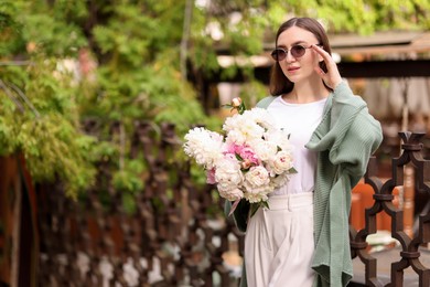 Photo of Charming woman with bouquet of beautiful peonies on city street. Space for text